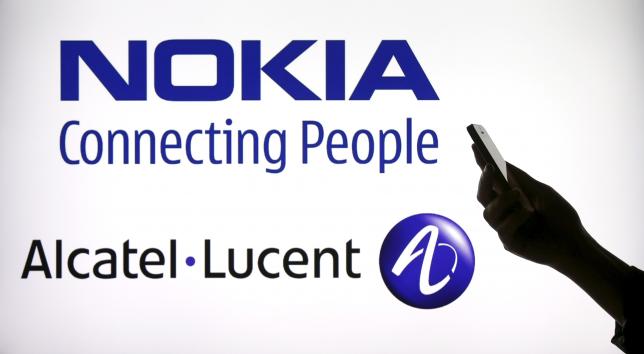 Photo illustration of a woman holding a smartphone in front of a screen displaying both Nokia and Alcatel Lucent logos in Paris